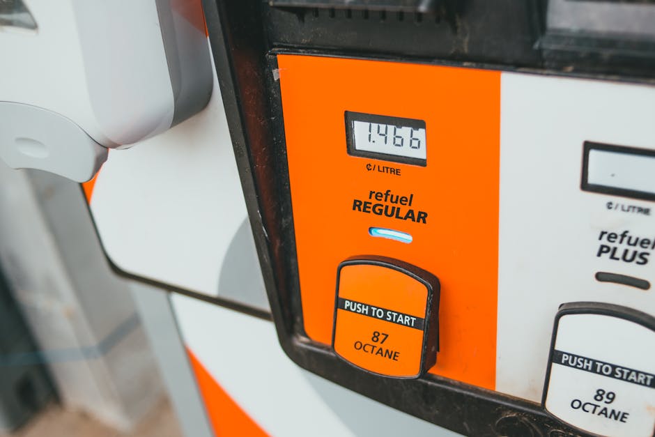 Close-up image of a petrol pump showing a digital display reading 1.486 litres of fuel. The fuel pump is predominantly orange with black and white accents, featuring a 'refuel REGULAR' label and a pus